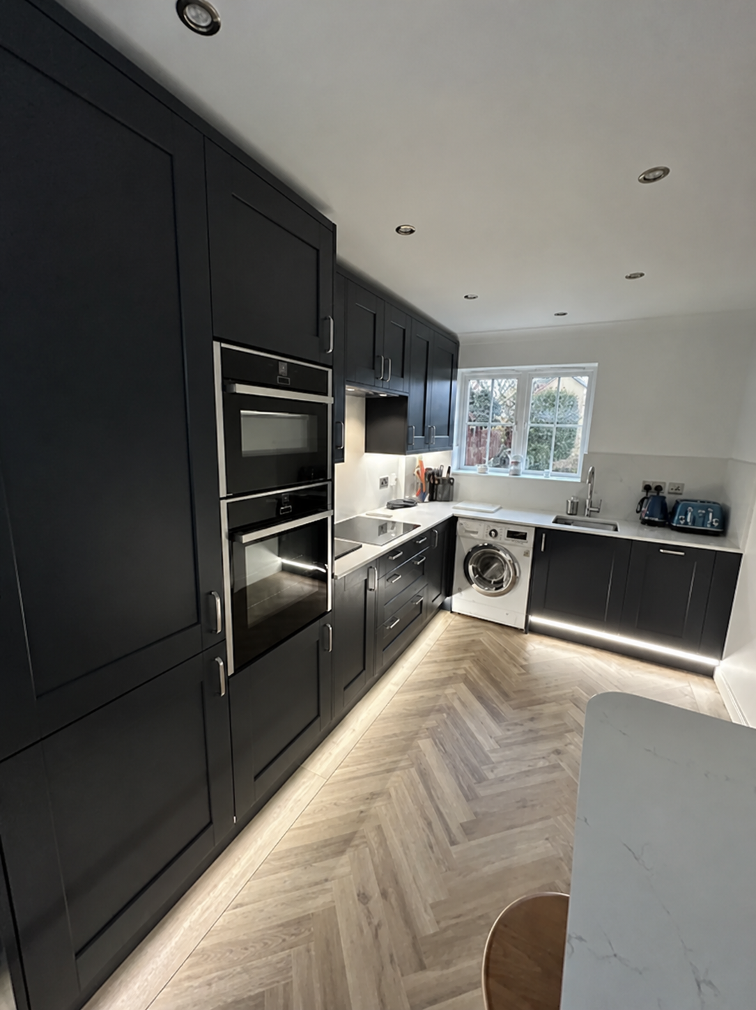 Matte black shaker kitchen with herringbone floor, white quartz worktops, under-unit LED lighting and integrated appliances
