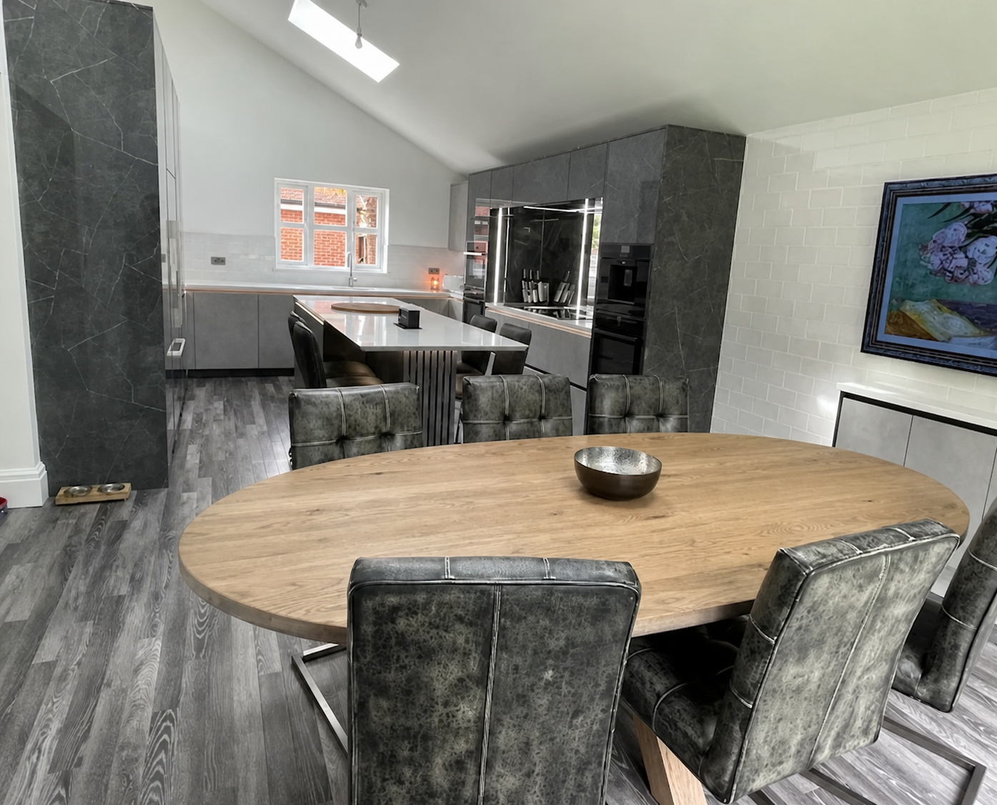 Open-plan grey marble-effect kitchen diner with oak table and a vaulted ceiling skylight
