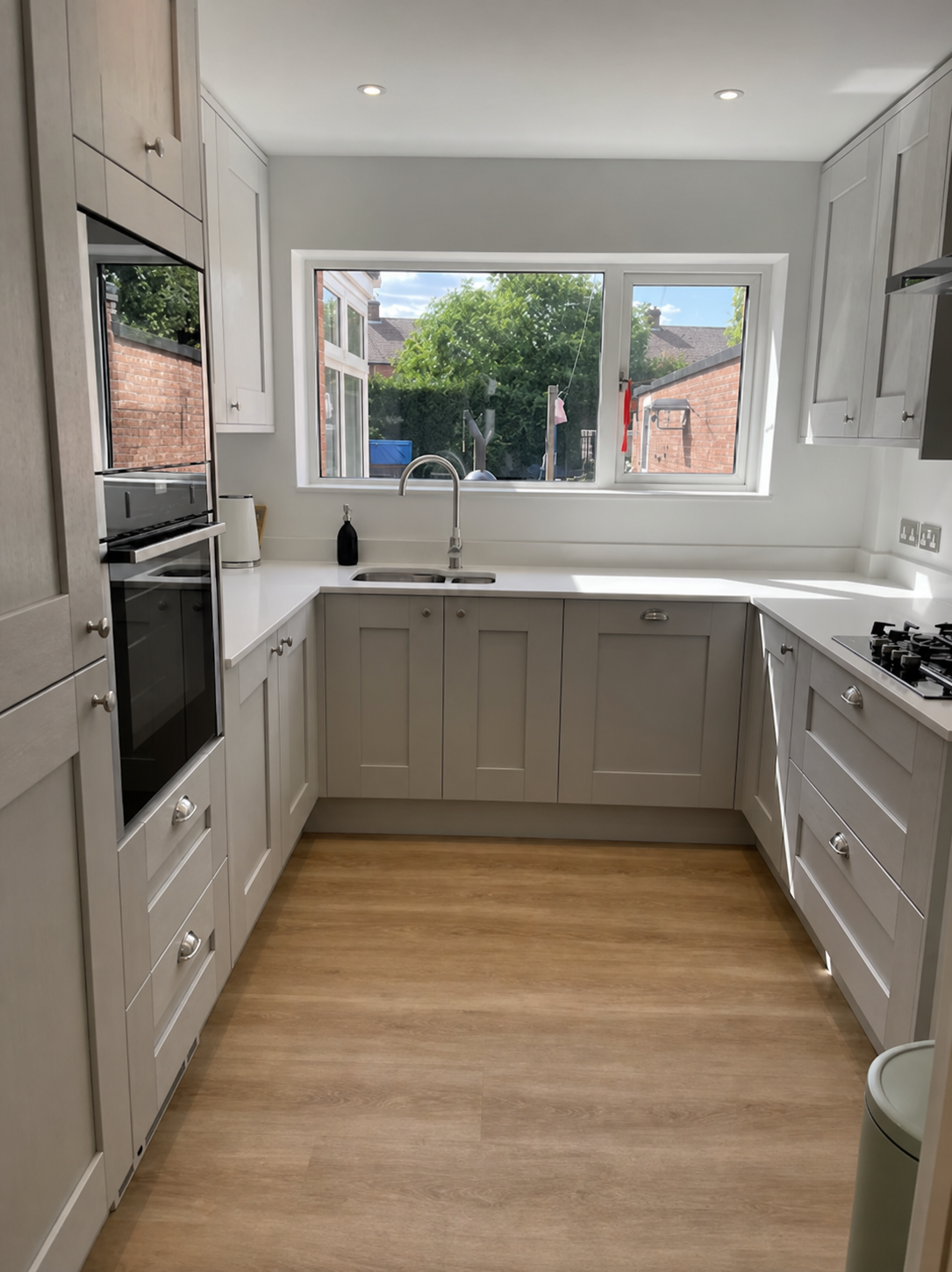 Bright light-greige U-shaped shaker kitchen with a window over the sink looking onto the garden