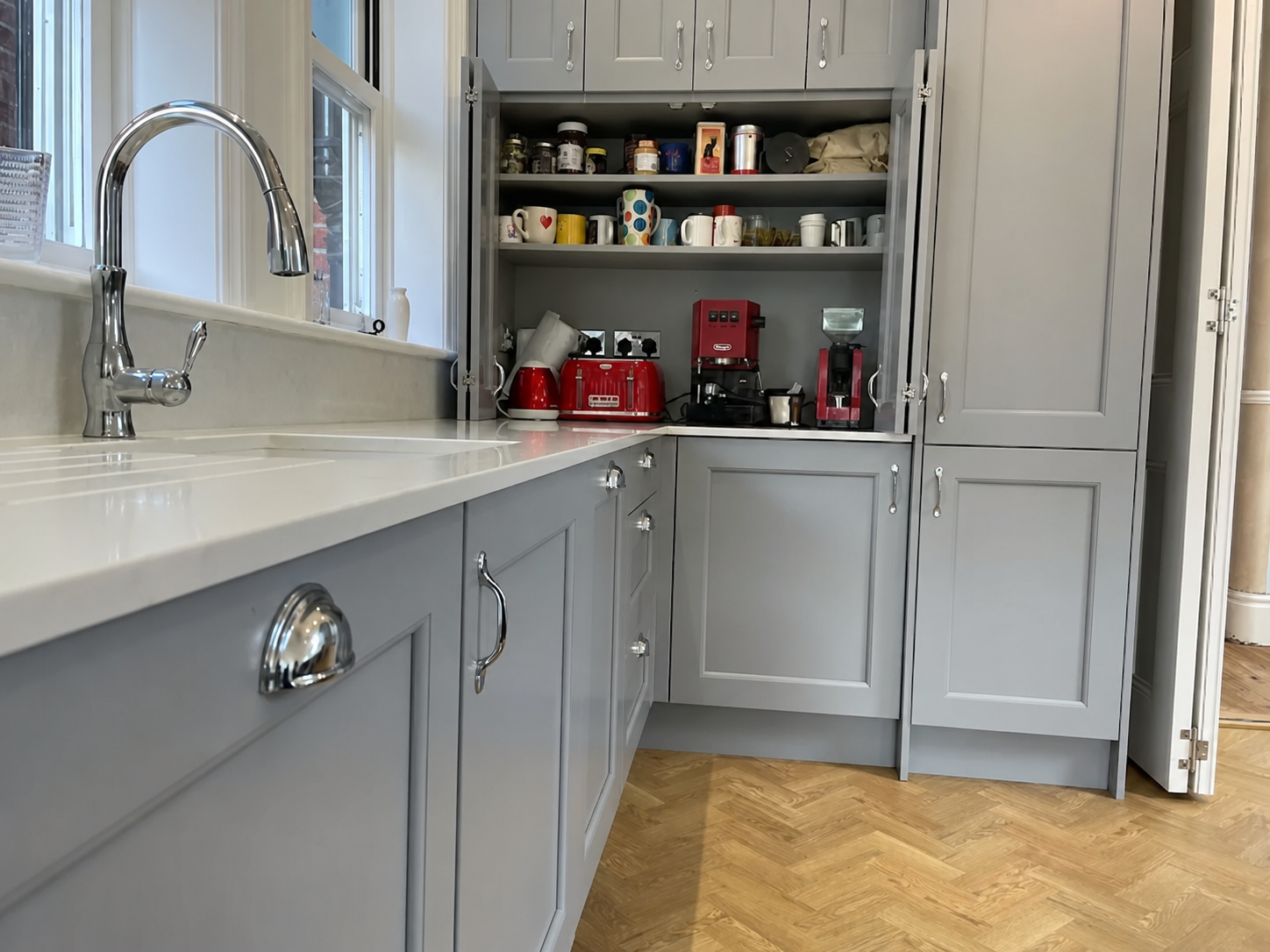 Bespoke fitted kitchen renovation in Basildon, Essex — light grey shaker cabinetry with chrome handles, quartz worktops and parquet flooring