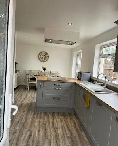 Completed grey shaker kitchen with open dining through, butcher-block worktop and recessed lighting